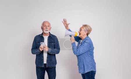 Femme âgée criant sur mégaphone à mari choqué en utilisant un téléphone intelligent sur fond blanc