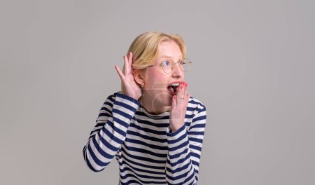 Photo for Excited shocked young woman covering her mouth with hand while listening gossip on white background - Royalty Free Image