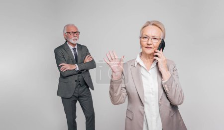Téléchargez les photos : Femme d'affaires senior parlant sur téléphone intelligent et refusant d'écouter homme d'affaires sur fond blanc - en image libre de droit