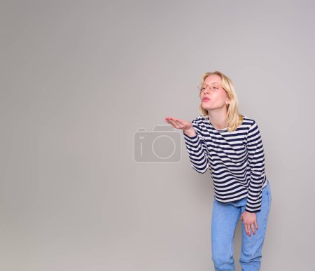 Beautiful woman blowing a kiss and looking away while flirting against isolated white background