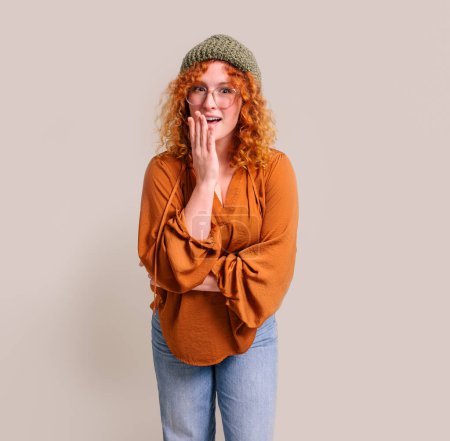 Portrait of shocked young beautiful woman covering mouth with hand and standing on white background