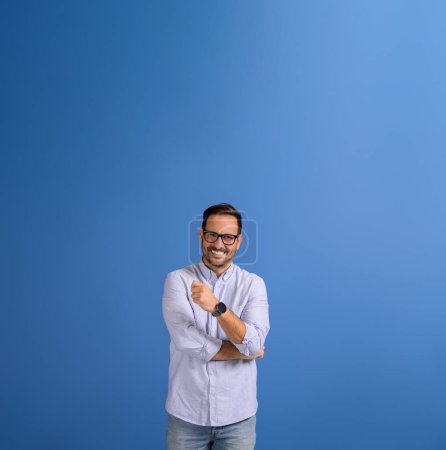 Retrato de joven y guapo gerente en gafas sonriendo a la cámara mientras está de pie sobre fondo azul