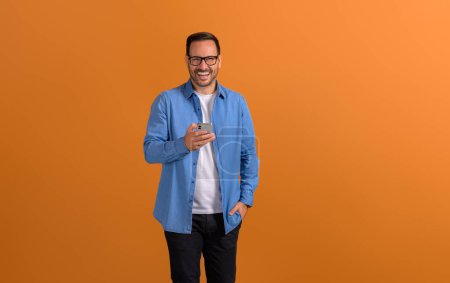 Männliche Profis lachen und checken Social-Media-Apps per Handy auf orangefarbenem Hintergrund
