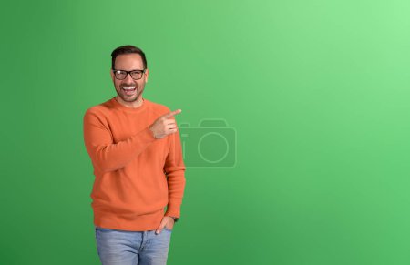 Porträt eines fröhlichen Verkäufers, der auf leeren Raum zeigt und auf grünem Hintergrund ein neues Produkt vermarktet