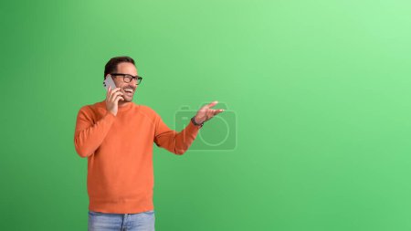 Photo for Young cheerful businessman sharing good news over phone call and gesturing against green background - Royalty Free Image