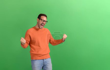 Young businessman with eyes closed screaming ecstatically and shaking fists over green background