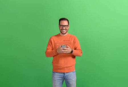 Lächelnder gutaussehender Manager nutzt soziale Medien per Smartphone, während er auf grünem Hintergrund steht