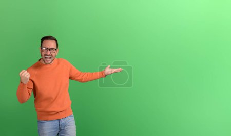 Portrait of excited businessman shaking fist and presenting new product on isolated green background