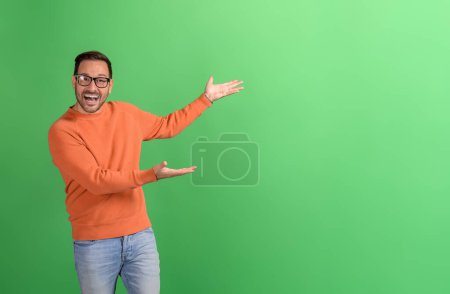 Joyful young businessman advertising new product with hands on copy space over green background