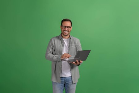 Portrait d'un beau freelance confiant faisant des recherches en ligne sur ordinateur portable sur fond vert