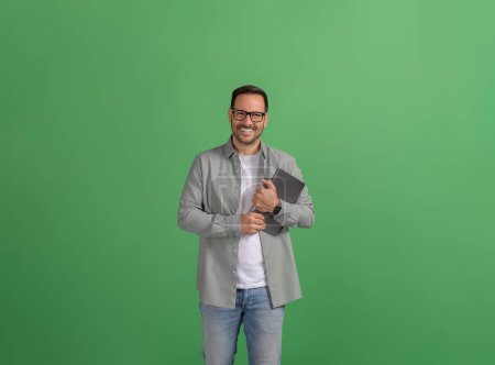 Schöner Jungunternehmer mit digitalem Tablet posiert selbstbewusst über isoliertem grünem Hintergrund