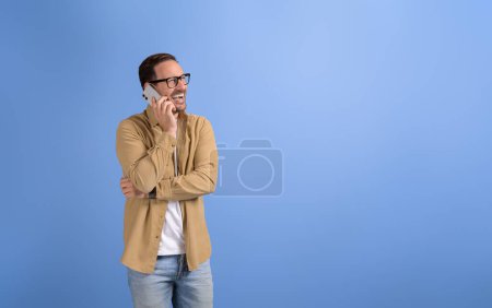 Photo for Portrait of young businessman laughing and communicating over mobile phone against blue background - Royalty Free Image