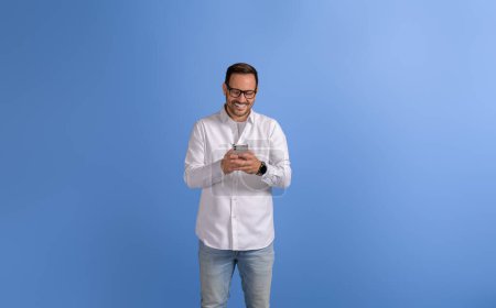 Portrait de souriant homme entrepreneur textos en ligne sur téléphone mobile sur fond bleu isolé