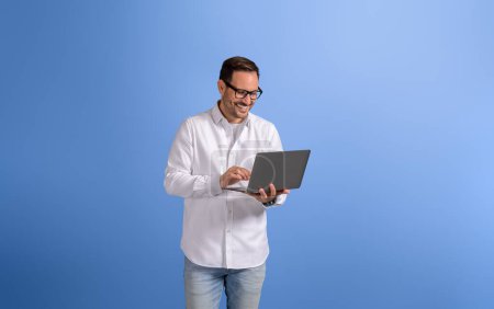 Portrait d'un bel entrepreneur vérifiant les e-mails sur un ordinateur sans fil sur fond bleu