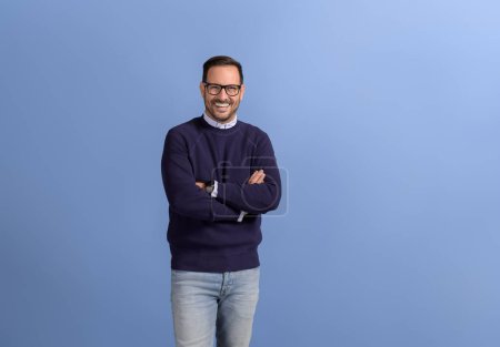 Portrait of handsome businessman with arms crossed posing confidently on isolated blue background