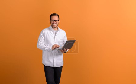 Portrait d'un homme d'affaires confiant effectuant des recherches en ligne sur un ordinateur sans fil sur fond orange