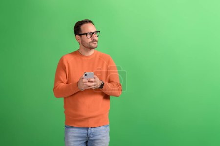 Jeune homme d'affaires utilisant le téléphone mobile et contemplant tout en regardant loin sur fond vert