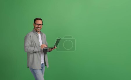 Succès heureux gestionnaire masculin travaillant sur ordinateur portable tout en se tenant avec confiance sur fond vert