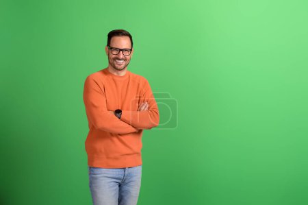 Portrait of young businessman smiling with arms crossed and posing confidently on green background
