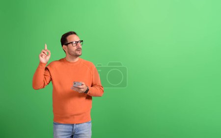 Porträt eines jungen Verkäufers, der sein Handy benutzt und auf den Kopierraum auf grünem Hintergrund zeigt