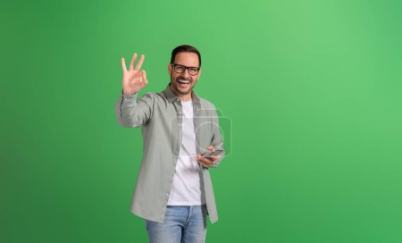 Retrato del hombre de negocios mostrando signo OK y compartiendo retroalimentación de aplicaciones móviles sobre fondo verde