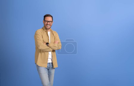 Portrait of confident sales manager with arms crossed smiling and posing on isolated blue background
