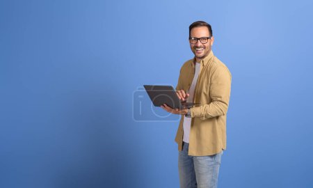 Portrait de jeune gestionnaire confiant analysant le rapport financier sur ordinateur portable sur fond bleu