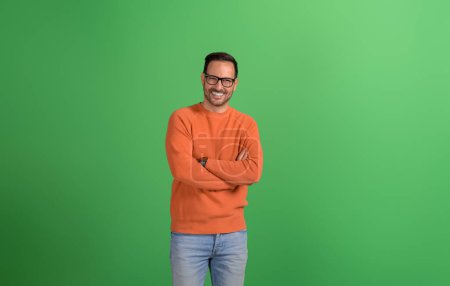 Young handsome entrepreneur standing with arms crossed and smiling at camera on green background