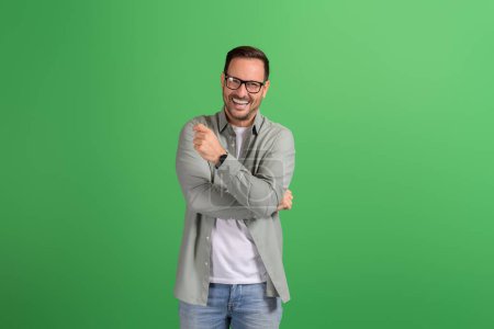 Portrait of young handsome professional confidently smiling at camera and posing on green background