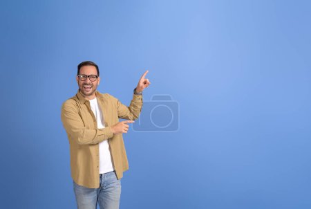 Porträt eines jungen Geschäftsmannes, der lacht und auf Kopierfläche für Werbung auf blauem Hintergrund abzielt