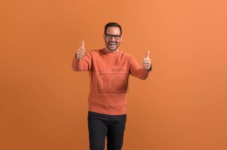 Aufgeregter Geschäftsmann lacht, zeigt Daumen hoch und feiert Erfolg auf orangefarbenem Hintergrund