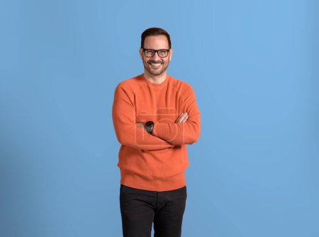 Portrait of male entrepreneur with arms crossed smiling and posing confidently over blue background