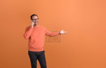 Ecstatic male entrepreneur sharing good news over phone call and gesturing against orange background