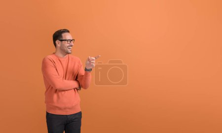 Happy young businessman pointing at empty space and demonstrating new product on orange background