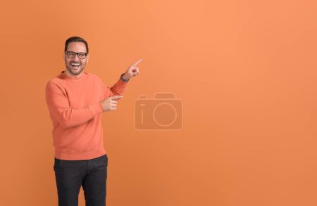 Porträt eines männlichen Promoters, der lacht und auf Kopierraum zeigt, während Marketing auf orangefarbenem Hintergrund