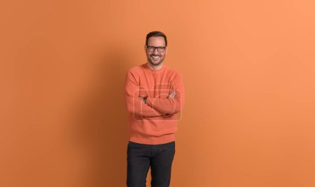 Porträt eines entschlossenen jungen Geschäftsmannes mit verschränkten Armen, der selbstbewusst auf orangefarbenem Hintergrund posiert
