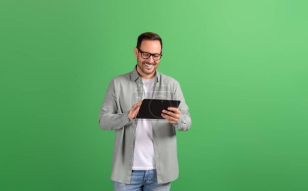 Foto de Joven hombre de negocios sonriente en anteojos leyendo e-mails sobre tableta digital sobre fondo verde - Imagen libre de derechos