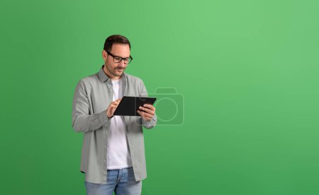 Focalisé jeune homme d'affaires faisant des recherches en ligne sur tablette numérique sur fond vert isolé