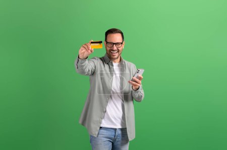 Businessman showing credit card and using online shopping apps over smart phone on green background