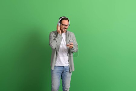 Lächelnder junger Mann mit Handy und Anrufen über Kopfhörer auf grünem Hintergrund