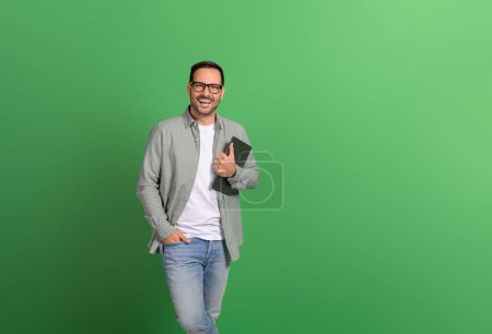 Porträt eines glücklichen Unternehmers mit der Hand in der Tasche, Laptop über isoliertem grünem Hintergrund