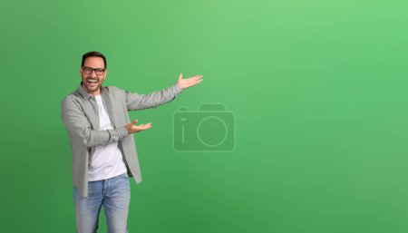 Young businessman laughing and presenting new product on empty space over isolated green background
