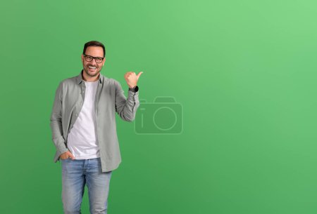 Porträt eines Verkäufers, der mit dem Daumen auf Kopierraum zielt und neues Produkt auf grünem Hintergrund demonstriert