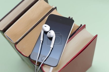 Téléchargez les photos : Téléphone avec écouteurs blancs sur pile de livres livre audio storytel podcast music concept copyspace - en image libre de droit