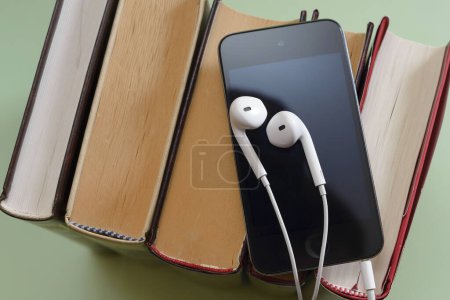 Foto de Teléfono con auriculares blancos en la pila de libros audiolibro storytel podcast música concepto copyspace - Imagen libre de derechos