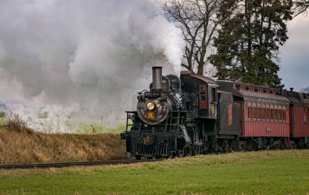Téléchargez les photos : Ronks, Pennsylvania, December 3, 2022 - A View of a Classic Steam Passenger Train, Blowing Lots of Smoke and Steam, While Traveling in the Countryside on an Autumn Day - en image libre de droit