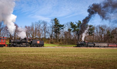 Foto de Ronks, Pennsylvania, December 4, 2022 - A View of Two Classic Steam Passenger Train, Blowing Lots of Smoke and Steam, While Traveling in the Countryside on an Autumn Day - Imagen libre de derechos