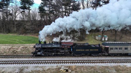 Photo for A Side Drone View of a Steam Locomotive Approaching Traveling Thru Fields and Meadows, Blowing White Smoke on a Winter Day - Royalty Free Image