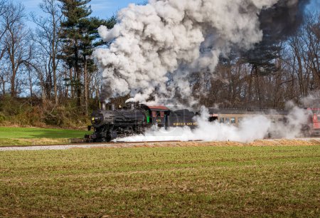 Foto de Ronks, Pennsylvania, December 4, 2022 - A View of a Classic Steam Passenger Train, Blowing Lots of Smoke and Steam, While Traveling in the Countryside on an Autumn Day - Imagen libre de derechos