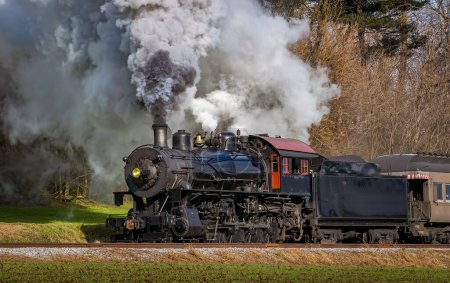 Téléchargez les photos : A View of a Classic Steam Passenger Train, Blowing Lots of Smoke and Steam, While Traveling in the Countryside on an Autumn Day - en image libre de droit